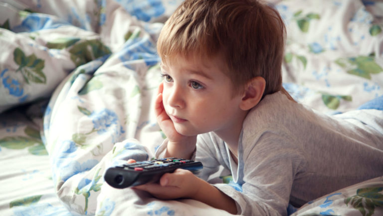 A little boy watches TV while holding the remote.