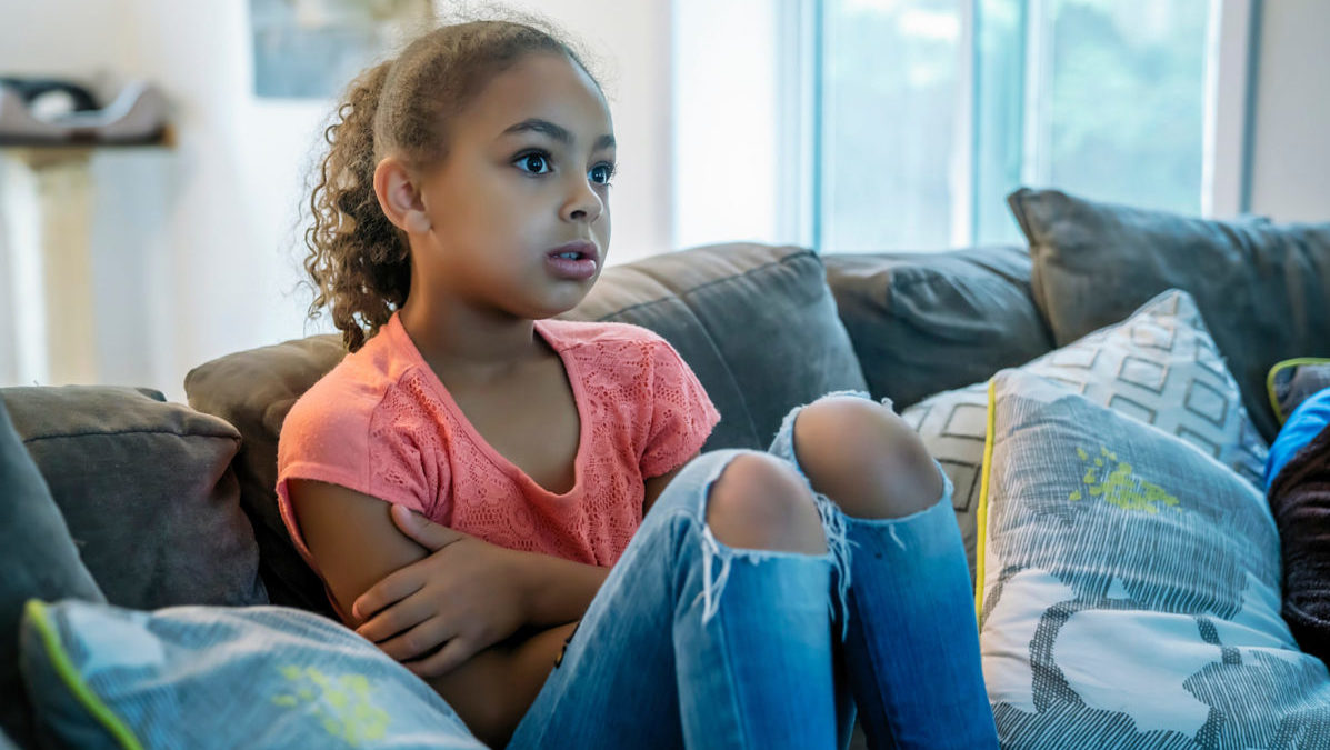 A little girl is visibly concerned while watching TV alone.