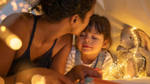 Loving mother kissing daughter in cozy hut.