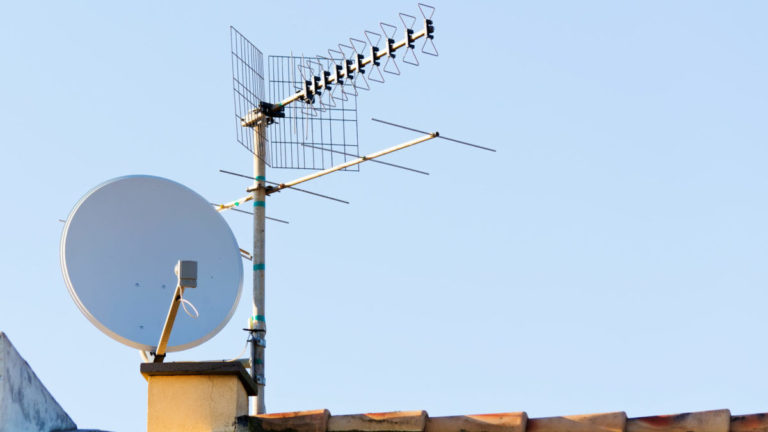 A satellite dish and TV antenna are together on a home's roof.