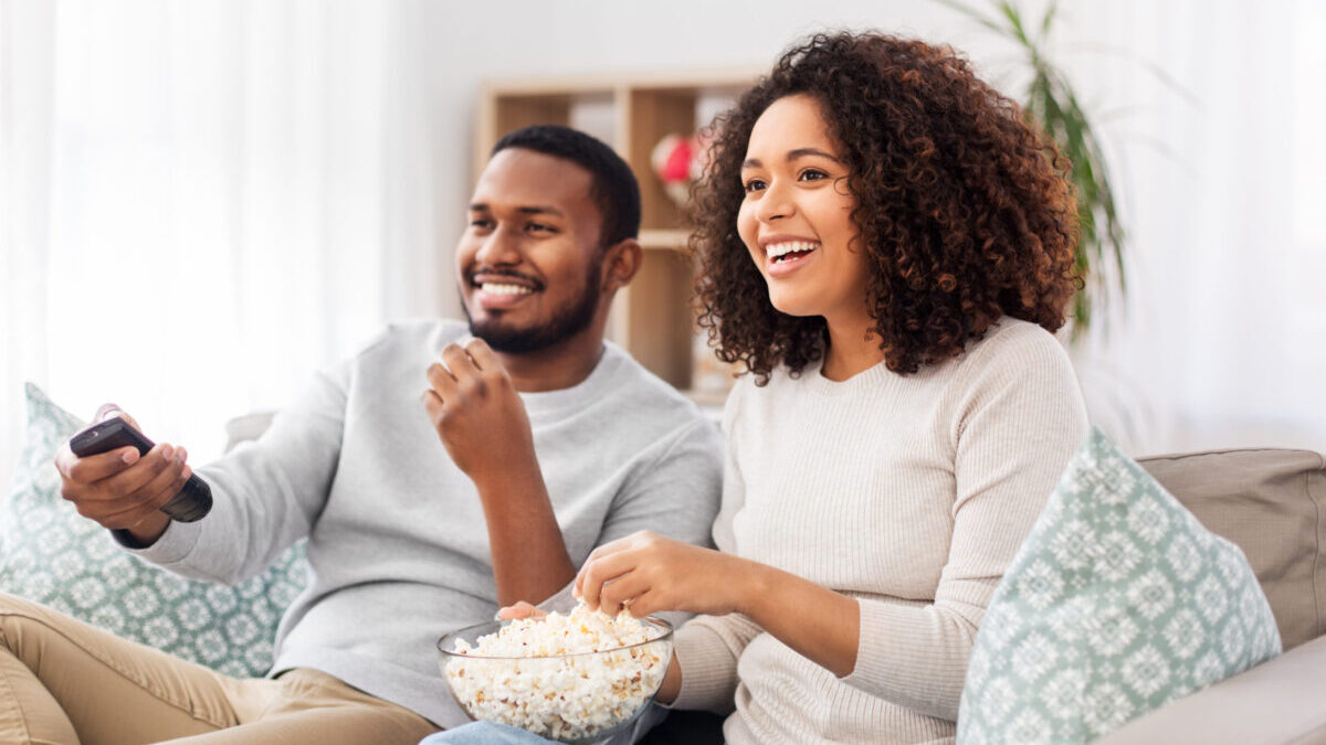 african couple with popcorn watching tv at home