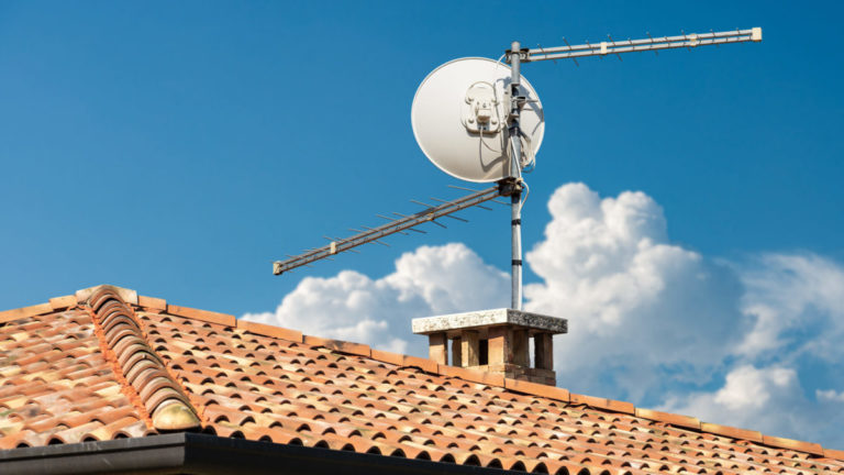 A stack of over-the-air TV antennas and a satellite dish sit atop a home's roof.